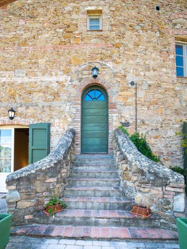 a stone building with a green door and stairs at Locanda Le Giunche in Guardistallo