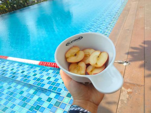 una persona sosteniendo una taza de plátanos frente a una piscina en Studio Healing at Sayana Apartemen Harapan Indah Bekasi, 