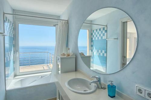 łazienka z lustrem, umywalką i oknem w obiekcie Villa Sa Calma w mieście Begur