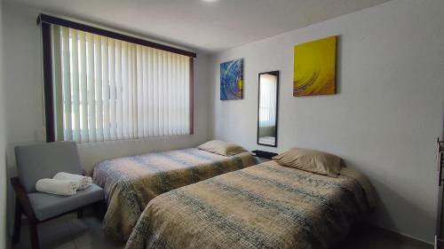 a bedroom with two beds and a chair and a window at Depa Balcones cerca Estadio GNP, Palacio de los Deportes, Autódromo HR y Aeropuerto CDMX in Mexico City