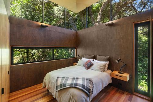 a bedroom with a large bed and large windows at Kawakawa House - Piha Holiday Home in Auckland