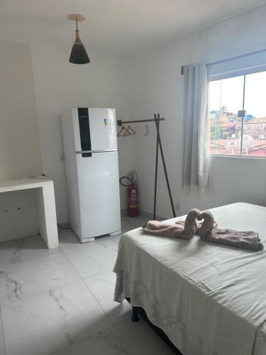 Cette chambre blanche comprend un lit et un réfrigérateur. dans l'établissement Suítes Modernas no Centro da Praia da Pipa, à Pipa