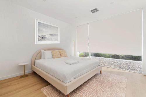 a white bedroom with a bed and a large window at Blanca Beach House 2 Vincentia in Vincentia