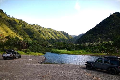 two trucks parked next to a river with mountains at Embark on a journey through Maui with Aloha Glamp's jeep and rooftop tent allows you to discover diverse campgrounds, unveiling the island's beauty from unique perspectives each day in Paia