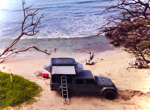 um jipe estacionado numa praia com uma tenda em Embark on a journey through Maui with Aloha Glamp's jeep and rooftop tent allows you to discover diverse campgrounds, unveiling the island's beauty from unique perspectives each day em Paia
