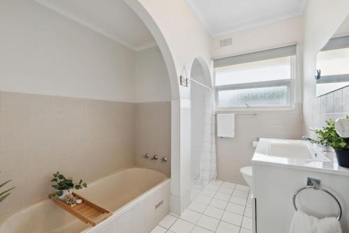 a white bathroom with a tub and a sink at Belle Escapes - Vitamin Sea at Henley Beach in Henley Beach