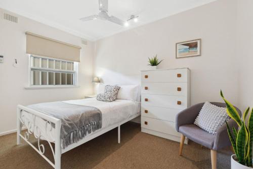 a white bedroom with a bed and a chair at Belle Escapes - Vitamin Sea at Henley Beach in Henley Beach