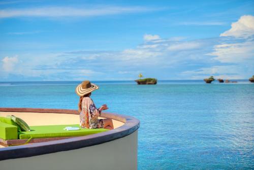 a woman in a hat sitting on a bench looking at the ocean at Koro Sun Resort & Rainforest Spa in Savusavu