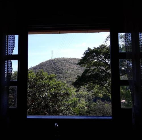 a window with a view of a hill with trees at Sossego entre as montanhas de Itaipava in Petrópolis