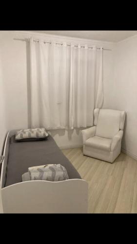a white bedroom with a bed and a chair at Apartamento próximo do aeroporto internacional in São José dos Pinhais