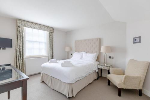 um quarto branco com uma cama grande e uma cadeira em Luxurious 3BD Flat - Sloane Square Chelsea! em Londres