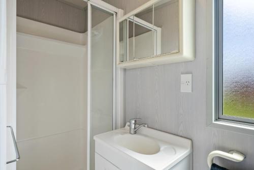 a white bathroom with a sink and a window at MGM Studio Cabin - Himitangi Holiday Studio in Foxton