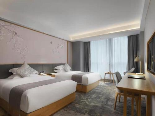 a hotel room with two beds and a desk at Baian Art Hotel Luzhou in Luzhou