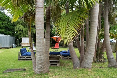 a patio with chairs and an umbrella between palm trees at Huriana Place in Kaitaia