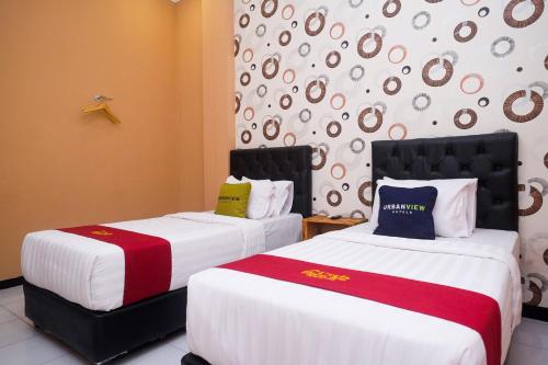 two beds in a hotel room with white and red sheets at Urbanview Hotel L'Tefa Pemalang in Padurekso