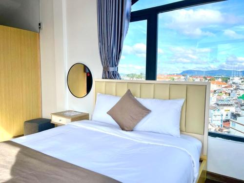 a bedroom with a white bed with a large window at Torino Hotel Dalat in Da Lat
