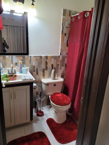 a bathroom with a toilet with a red shower curtain at Silverbuttons Apartments & Eats in Dickenson Bay
