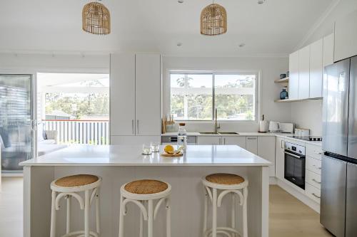a white kitchen with a large island with bar stools at beached at mollymook in Mollymook