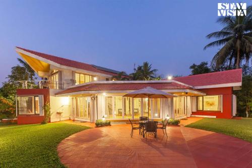 a house with a patio with chairs and an umbrella at StayVista's Waterway Retreat - Lakeside Oasis with Infinity Pool in Wada
