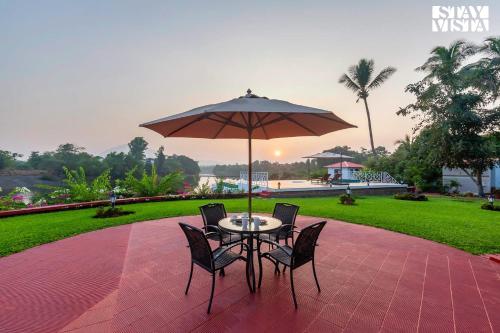 a table with chairs and an umbrella on a patio at StayVista's Waterway Retreat - Lakeside Oasis with Infinity Pool in Wada