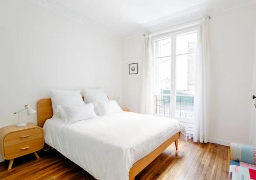 une chambre blanche avec un grand lit et une fenêtre dans l'établissement Charmant appartement près du Père Lachaise, à Paris