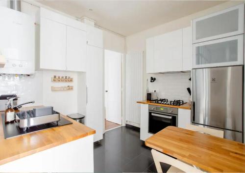 une cuisine avec des armoires blanches et un réfrigérateur en acier inoxydable dans l'établissement Charmant appartement près du Père Lachaise, à Paris