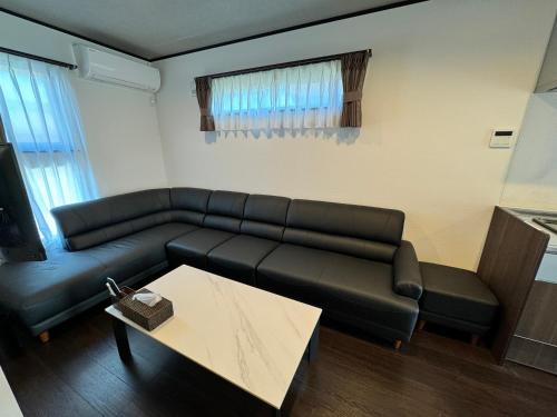 a living room with a black leather couch and a table at 温泉付き貸別荘 風車村 E-10 with hot spring in Takashima