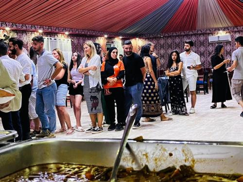 un grupo de personas de pie alrededor de una mesa comiendo comida en wadi rum guest house camp, en Áqaba