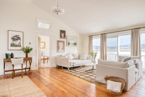 una sala de estar con muebles blancos y ventanas grandes. en River House by AvantStay Historic Secluded Estate on the Hudson River w Pool Sleeps 24, en Hudson