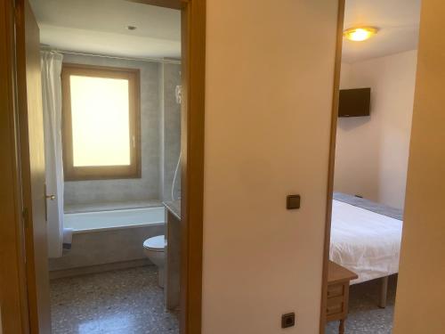 a bathroom with a toilet and a bed and a window at Hostal El Quintà in Espinavell