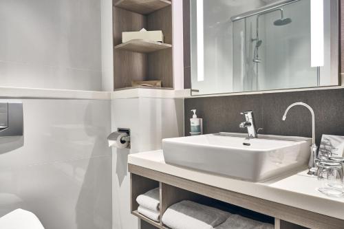 a white bathroom with a sink and a mirror at Novotel Singapore on Kitchener in Singapore