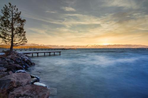 a lake with a pier and a tree on the shore at Tennenbaum by AvantStay Classic Cabin in Tahoe Vista - Walk to the Beach in Tahoe Vista