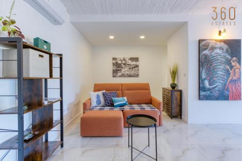 a living room with an orange couch and a stool at A lovely, central 2BR penthouse with large outdoor by 360 Estates in LʼInglin