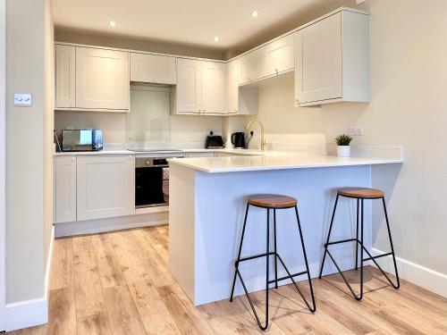 a kitchen with white cabinets and two bar stools at Barbican Loft - with Free parking in York