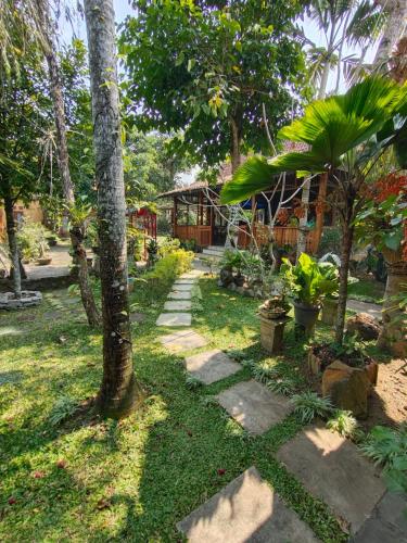 a path in a garden with trees and a house at Mettaloka Guesthouse in Magelang