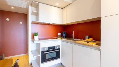 a kitchen with white cabinets and an orange wall at Résidence Kaliopé in Le Lavandou