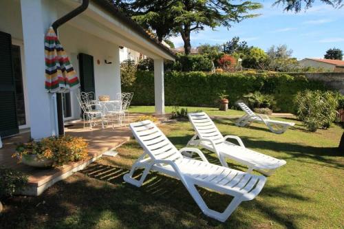 tre sedie da giardino bianche e un ombrellone in un cortile di Villa Margherita Bilocale - Taunus Vacanze a Numana