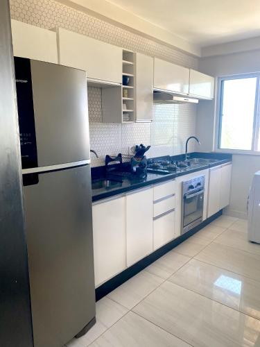 a kitchen with white cabinets and a stainless steel refrigerator at Apartamento Ilhéus - Vog Sul in Ilhéus