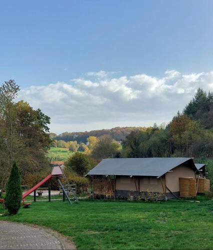 un edificio con tetto di paglia e parco giochi di Camping Drei Spatzen a Utscheid
