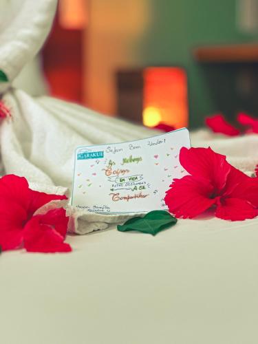 a card on a bed with red flowers on it at Igarakuê Flat in Japaratinga