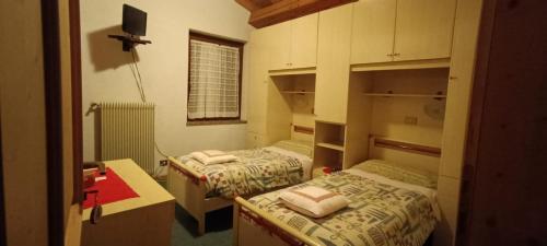 a bedroom with two beds and a desk and a television at Pizzeria Marmolada Camere in Sottoguda