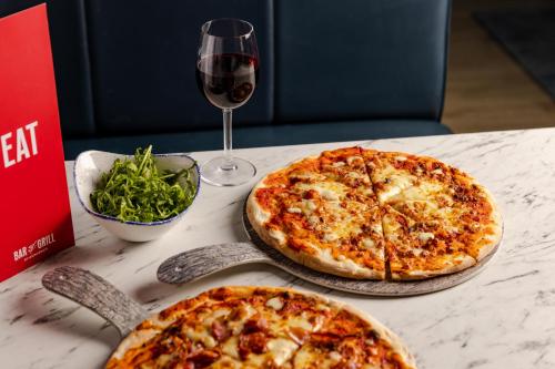 two pizzas sitting on a table with a glass of wine at Leonardo Hotel London Croydon in Croydon