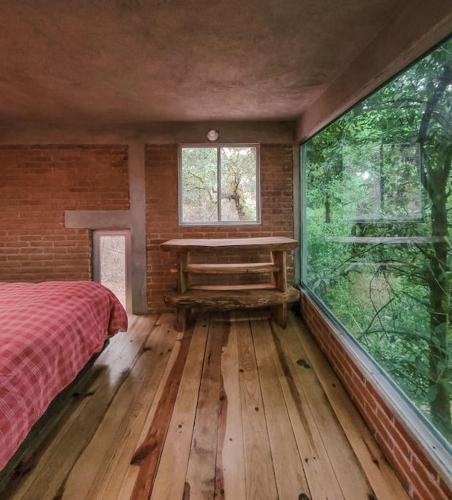 a bedroom with a bed and a window and a table at The Red Cabin at the bottom of Tepoztlán's Forest in Tepoztlán