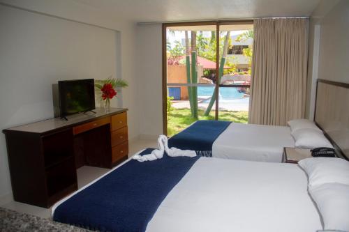 a bedroom with two beds and a tv and a window at Hotel Margarita Dynasty in Porlamar