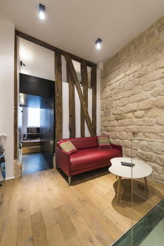 - un canapé rouge dans une chambre dotée d'un mur en pierre dans l'établissement Le Marais - Place des Vosges - Tournelles 86, à Paris