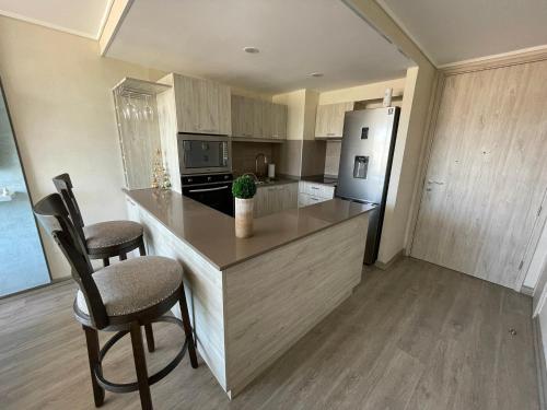 a kitchen with a island with two chairs and a refrigerator at Arriendo Departamento 10 Norte Viña del Mar in Viña del Mar