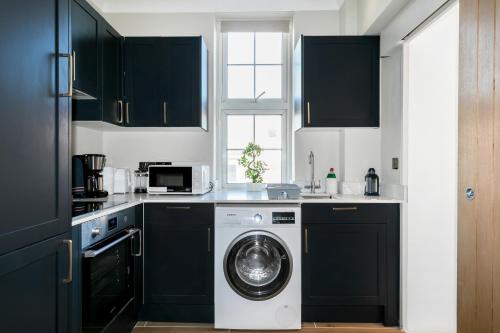 a kitchen with black cabinets and a washing machine at Bright One Bedroom Flats near Marble Arch and Hyde Park in London