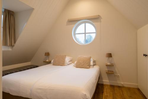 a bedroom with a white bed with a window at Villa Zuiderduin cottage in Zoutelande