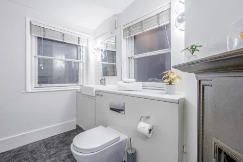 a white bathroom with a toilet and two windows at Tottenham Court's House - 2 Bed in London