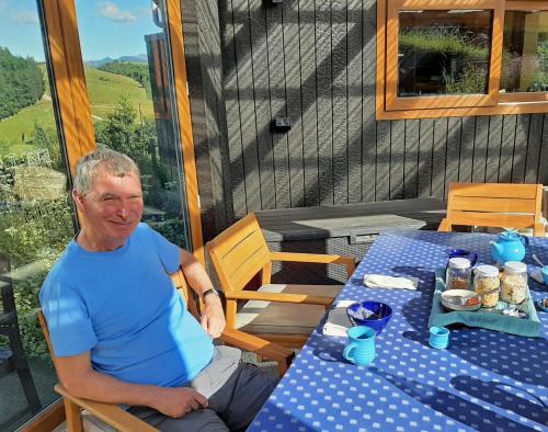 an older man sitting at a table on a porch at Kotare BandB in Geraldine